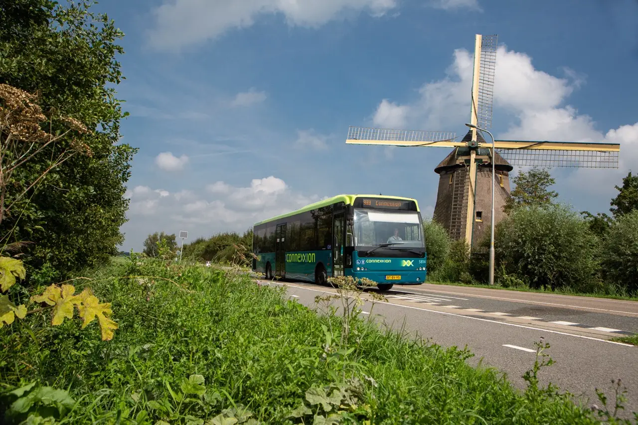 Foto van Connexxion-bus in landelijk gebied met een molen op de achtergrond