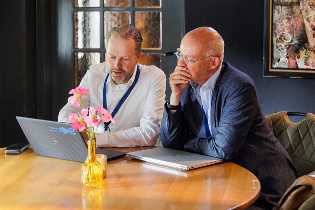 Foto van twee mannen aan tafel bezig op een laptop
