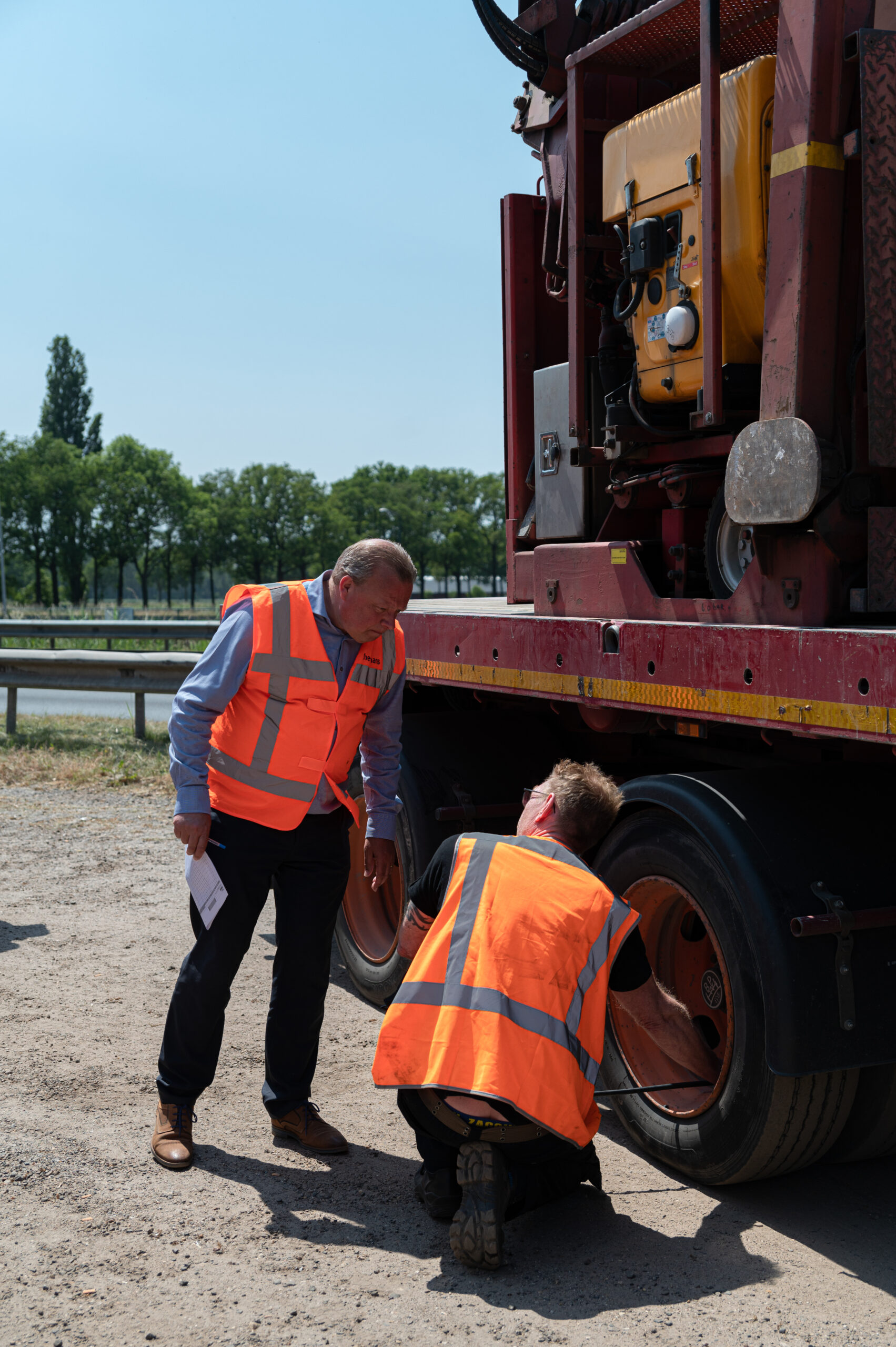 Foto van twee heren met oranje veiligheidshesjes aan die naast een grote truck staan en een bandencontrole doen